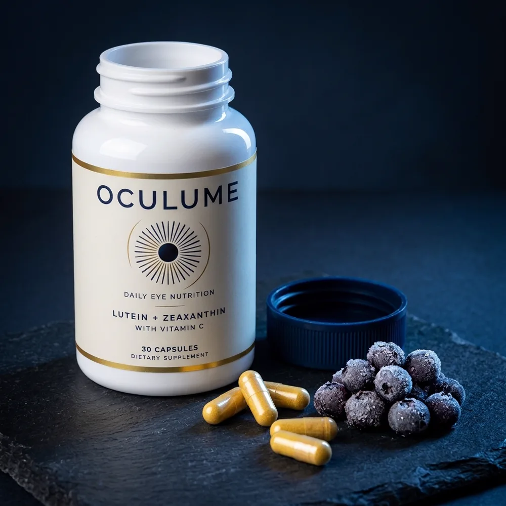 Oculume capsules spilling from the bottle next to frozen wild bilberries